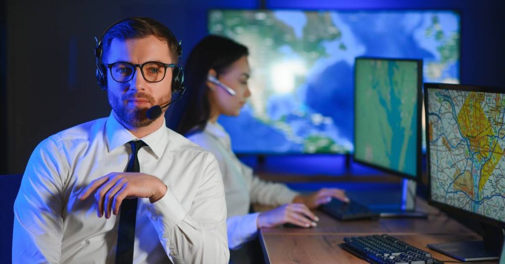 Two dispatchers sitting at a desk in a control room. One types on her keyboard, the other is turned away from his computer.