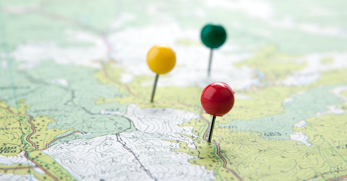 A close up of one green, one yellow, and one red push pin inserted into a topographic map.