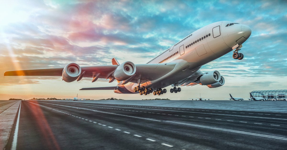 A large, double-decker, white airplane takes off from an airport runway on a partly cloudy day.